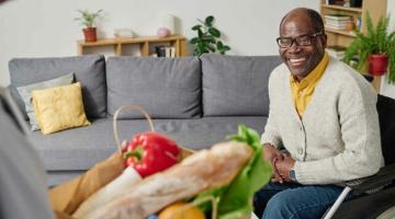 A man in a wheelchair accepts a parcel of groceries, he is happy