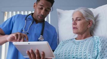 A male nurse with a woman with white hair view results on an iPad