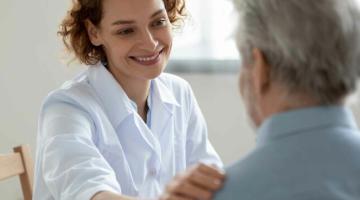 A woman with short red hair places a hand on an older man's shoulder. She is smiling