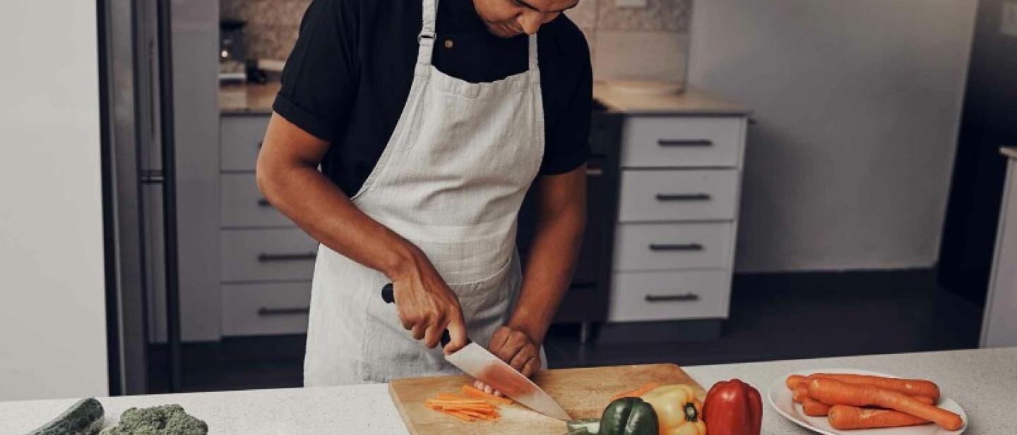 Aman wearing a white apron uses a knife to chop vegetables