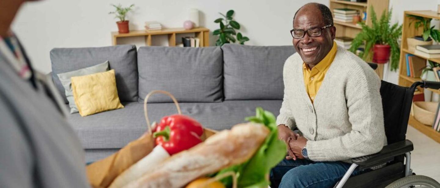 A man in a wheelchair accepts a parcel of groceries, he is happy