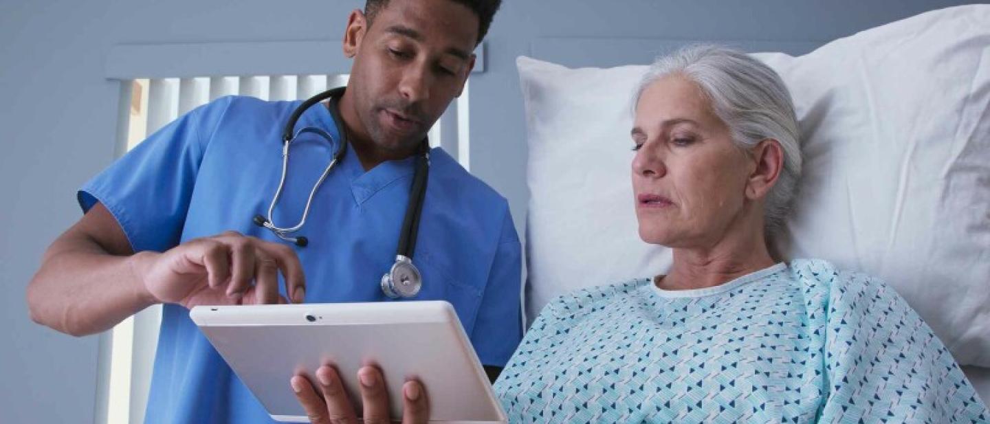 A male nurse with a woman with white hair view results on an iPad
