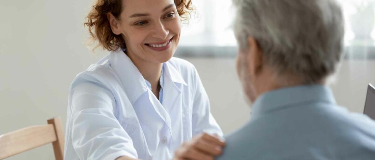 A woman with short red hair places a hand on an older man's shoulder. She is smiling