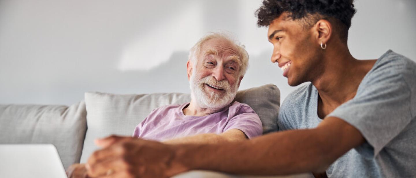 A young man laughs with an older man, as he shows him a laptop screen