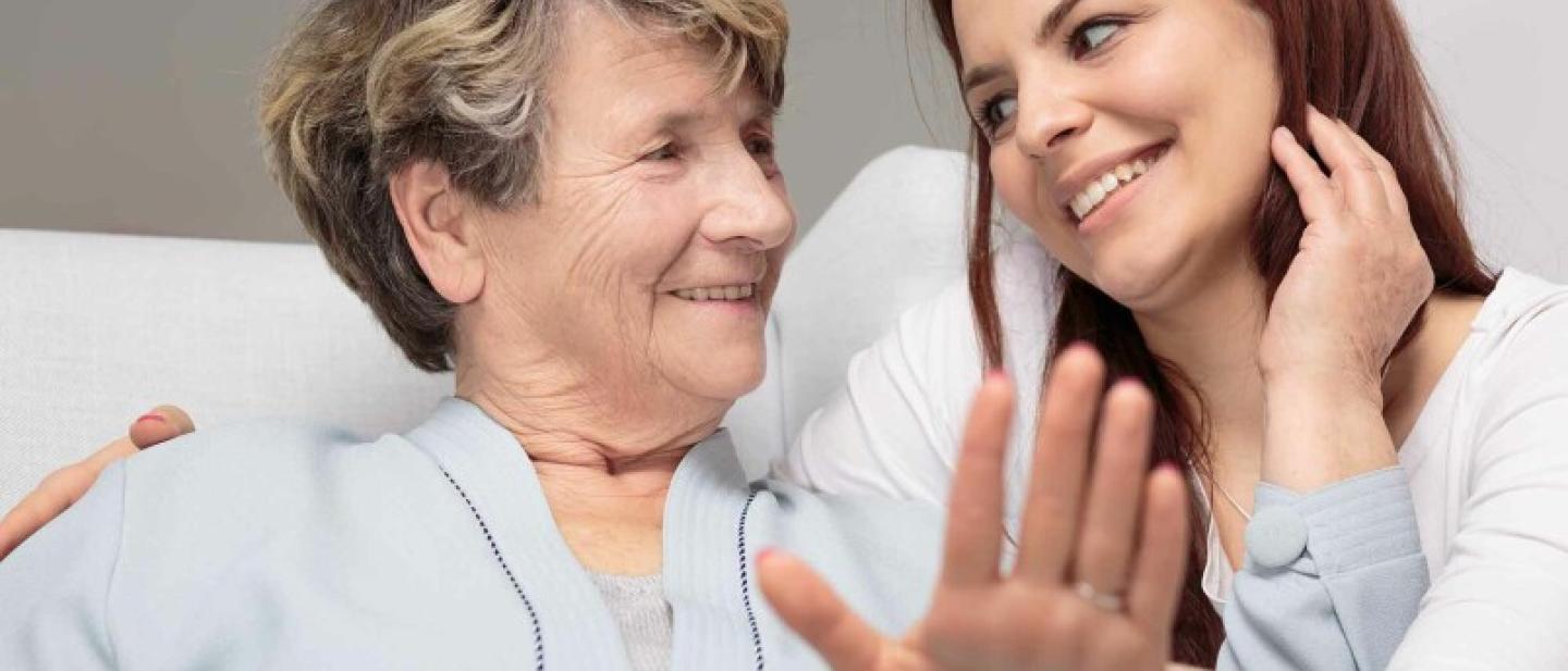 A younger woman is smiling, with her arm around an older woman